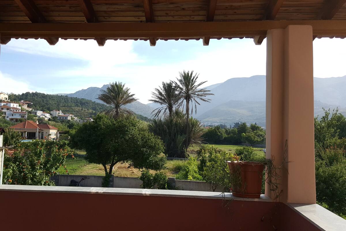 A balcony with a view of a residential area, palm trees, and mountains in the distance.
