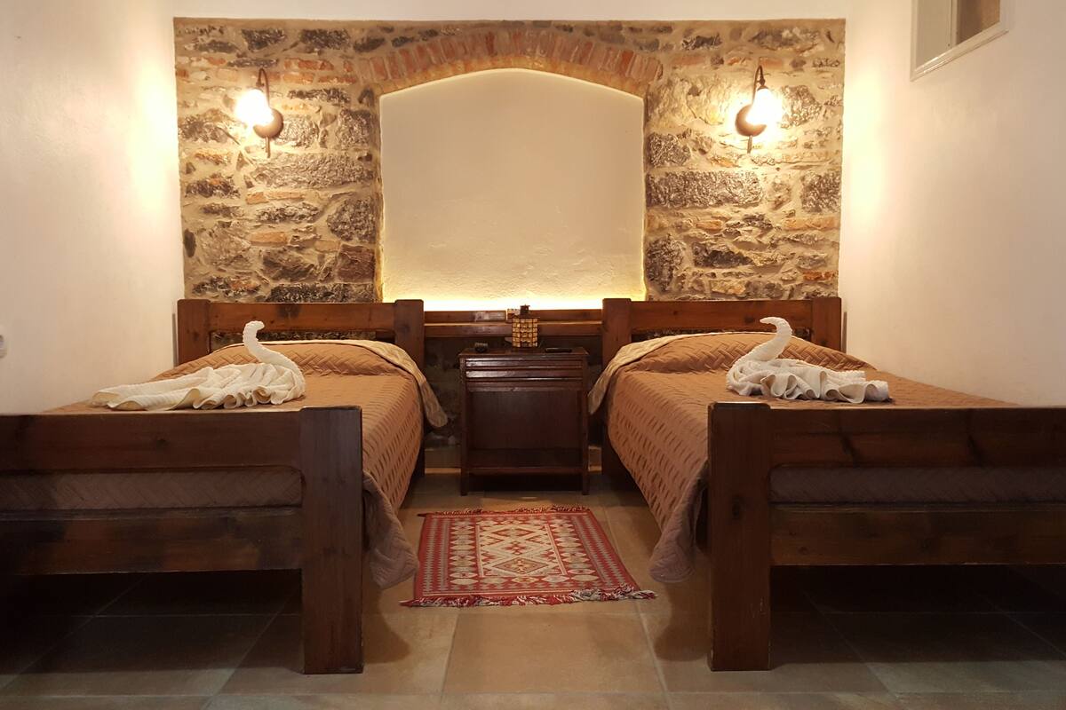 A room with two wooden beds, a stone wall, and a small table between them.