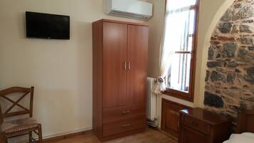 Ein Zimmer mit einem Holzschrank, einem an der Wand befestigten Fernseher, einem Fenster mit Vorhängen und einem Heizkörper.