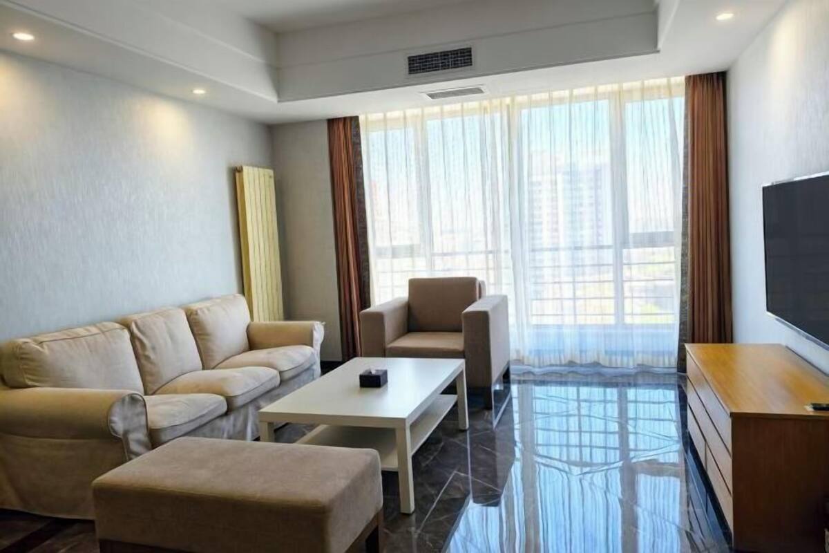 A modern hotel room with a sofa, armchair, coffee table, and a flat-screen TV.