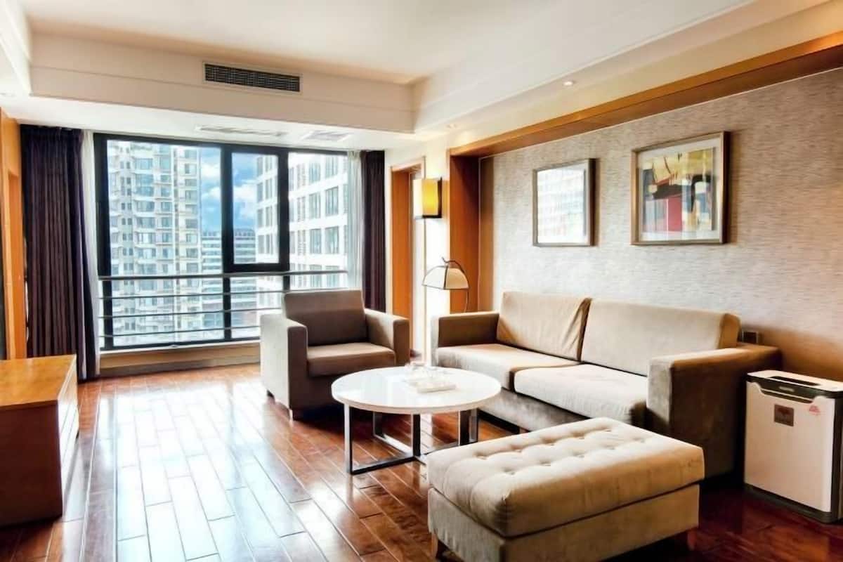 A modern hotel room with a sofa, armchair, ottoman, and a small table.
