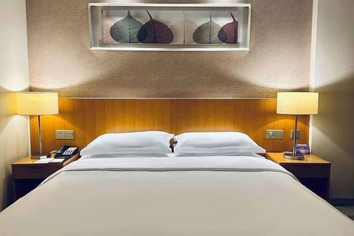 A hotel room with a bed, two bedside lamps, a phone, and a wall-mounted artwork.