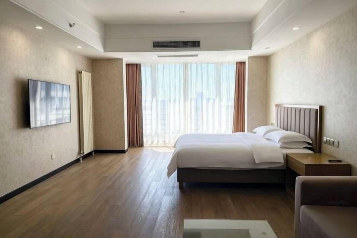 A hotel room with a large bed, a TV, a bedside table, and a window with curtains.