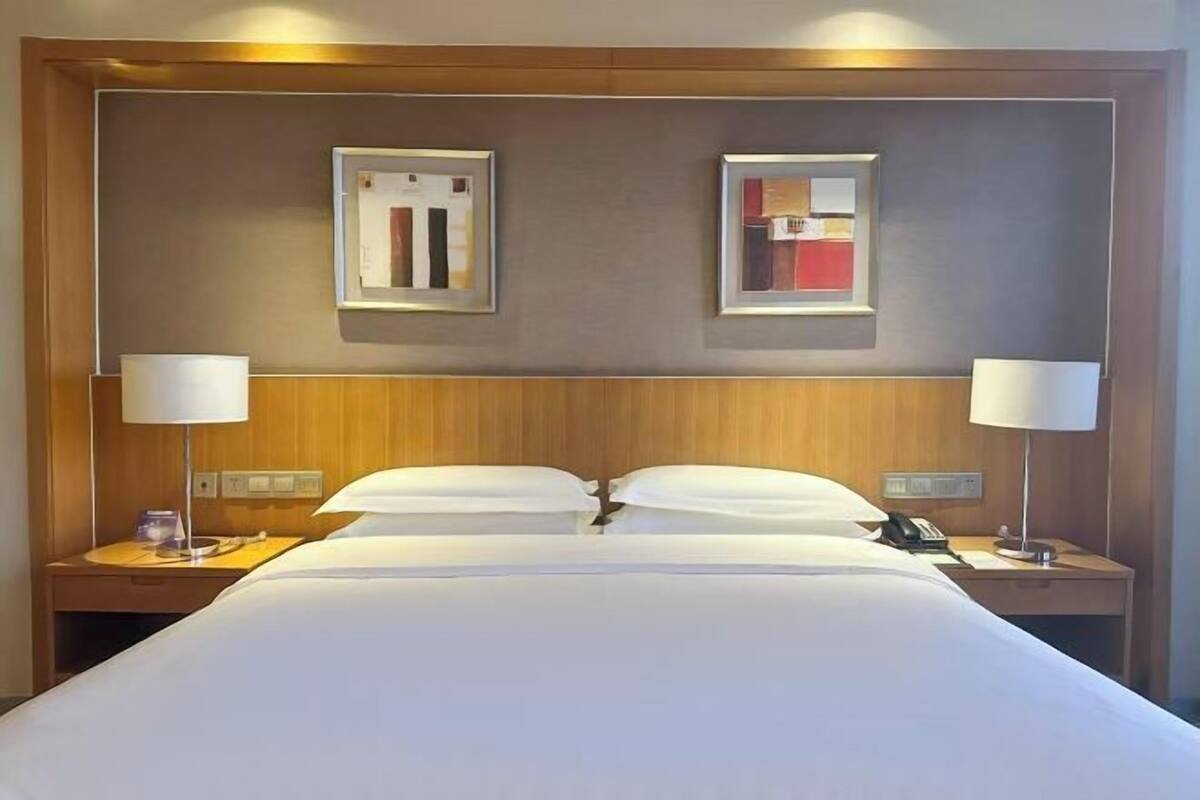 A hotel room with a large bed, two bedside tables, a nightstand, a lamp, and two framed pictures on the wall.