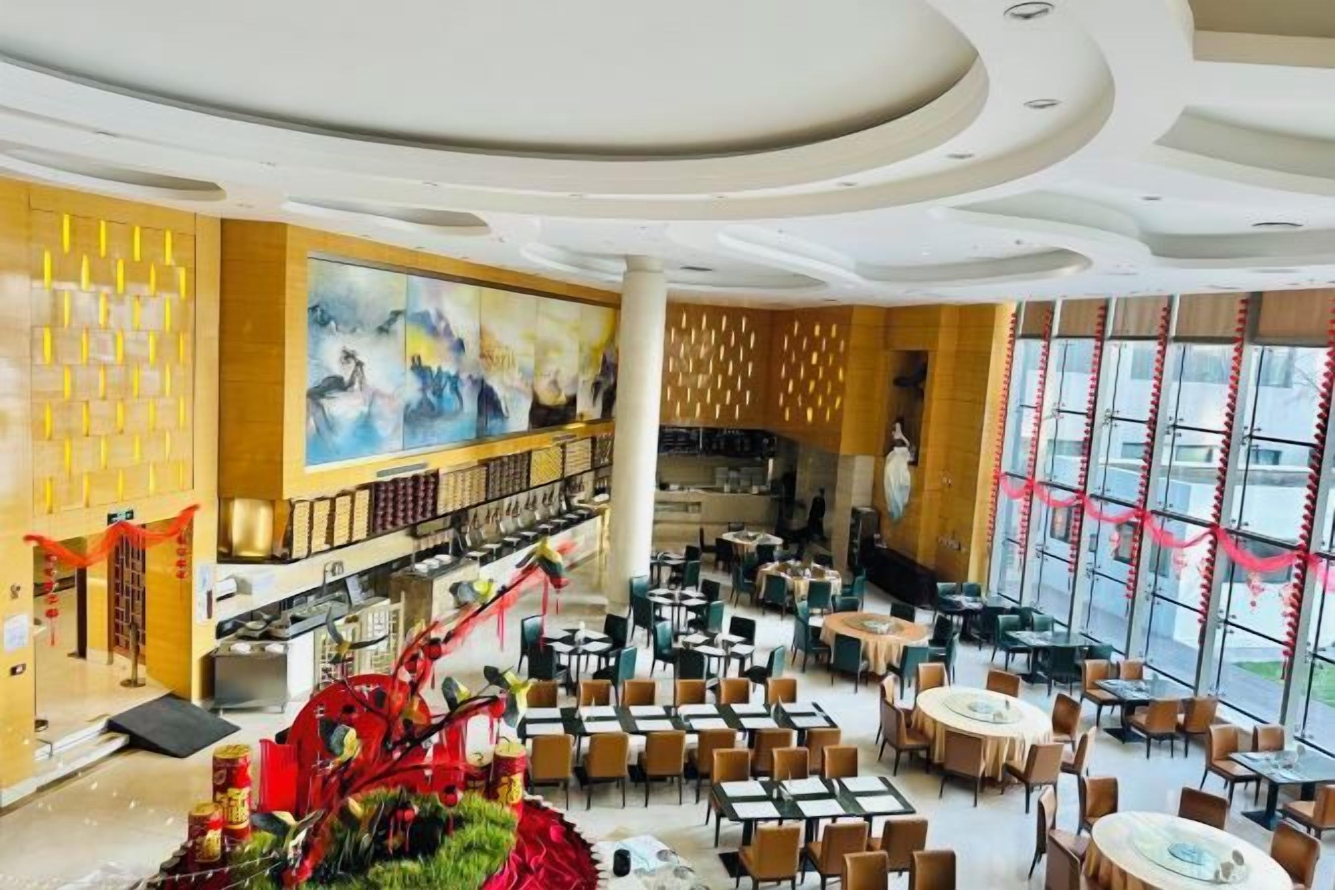 Eine geräumige Hotelhalle mit mehreren Gastronomiebereichen, einem großen Wandgemälde und einer Treppe.