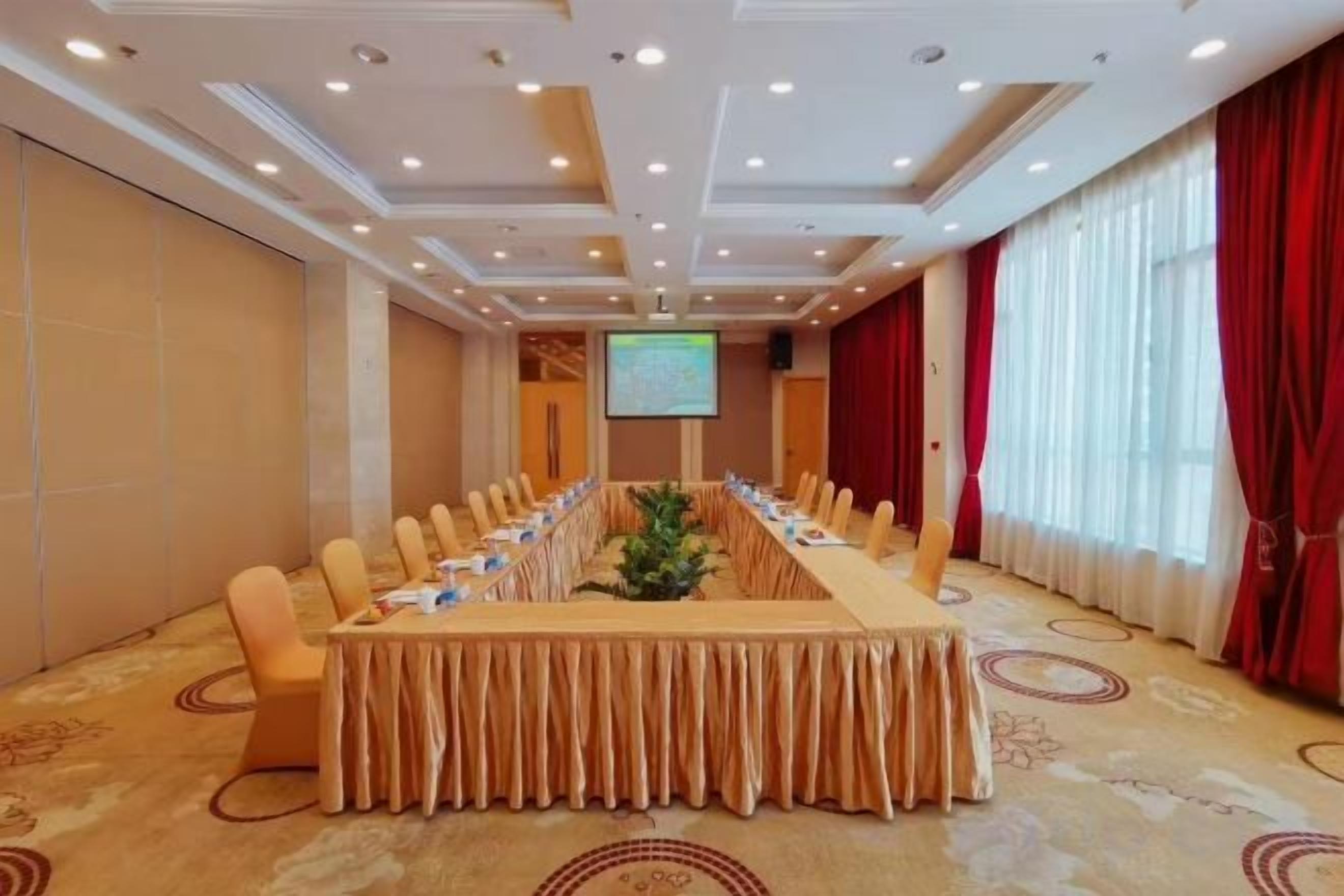 A conference room with a long table, chairs, a television screen, and a red curtain.
