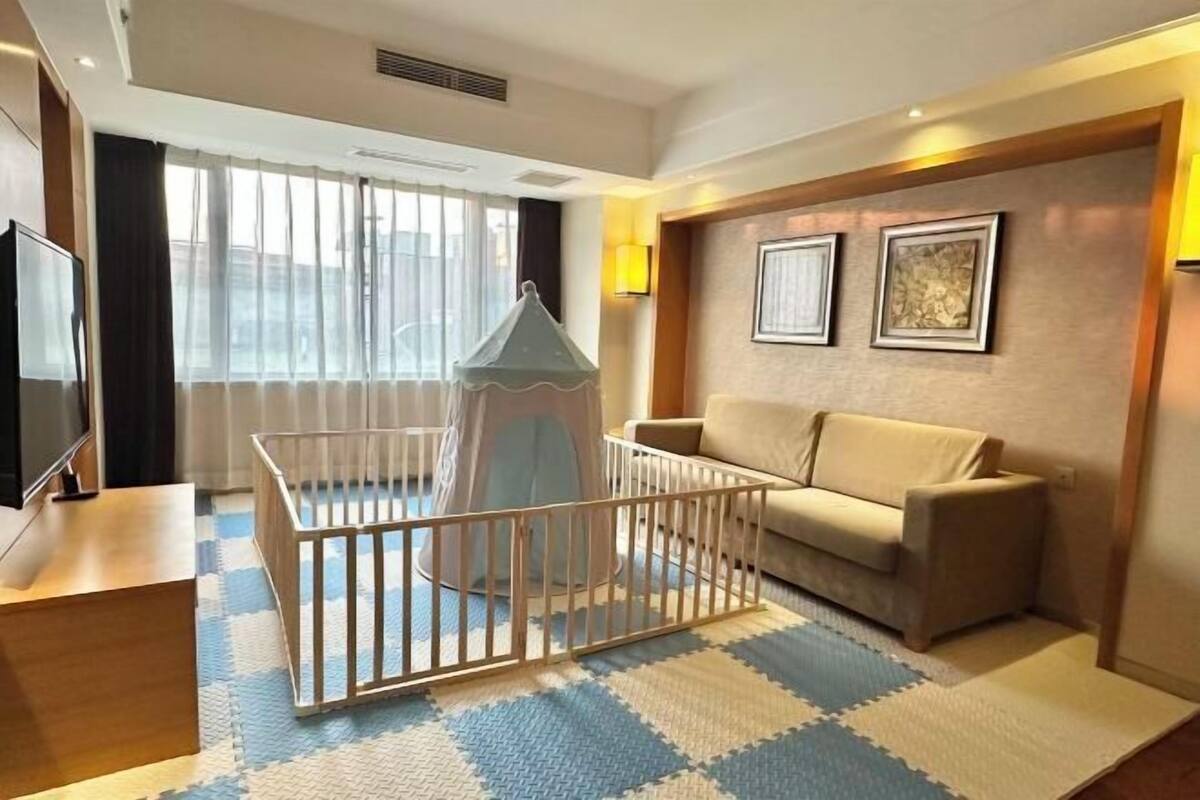 A hotel room with a crib, a sofa, a television, and framed artwork on the wall.