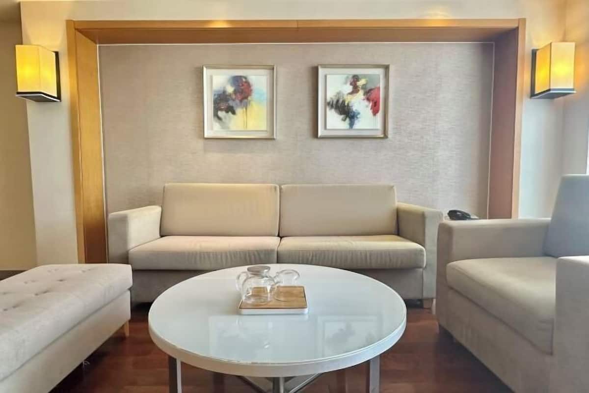 A modern living room with a sofa, armchairs, a coffee table, and two framed abstract paintings on the wall.