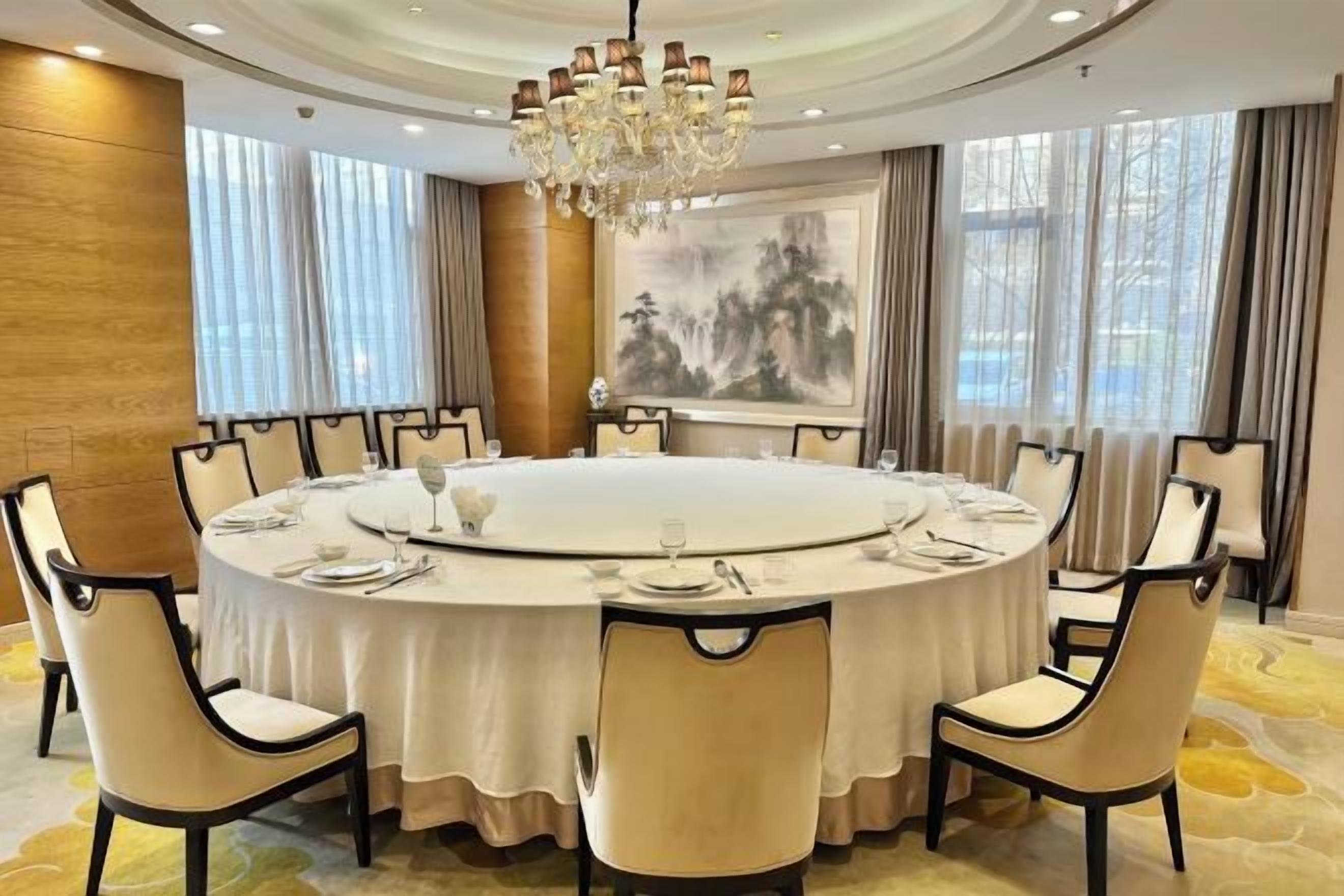 A round dining table with chairs, a chandelier, and a painting on the wall.