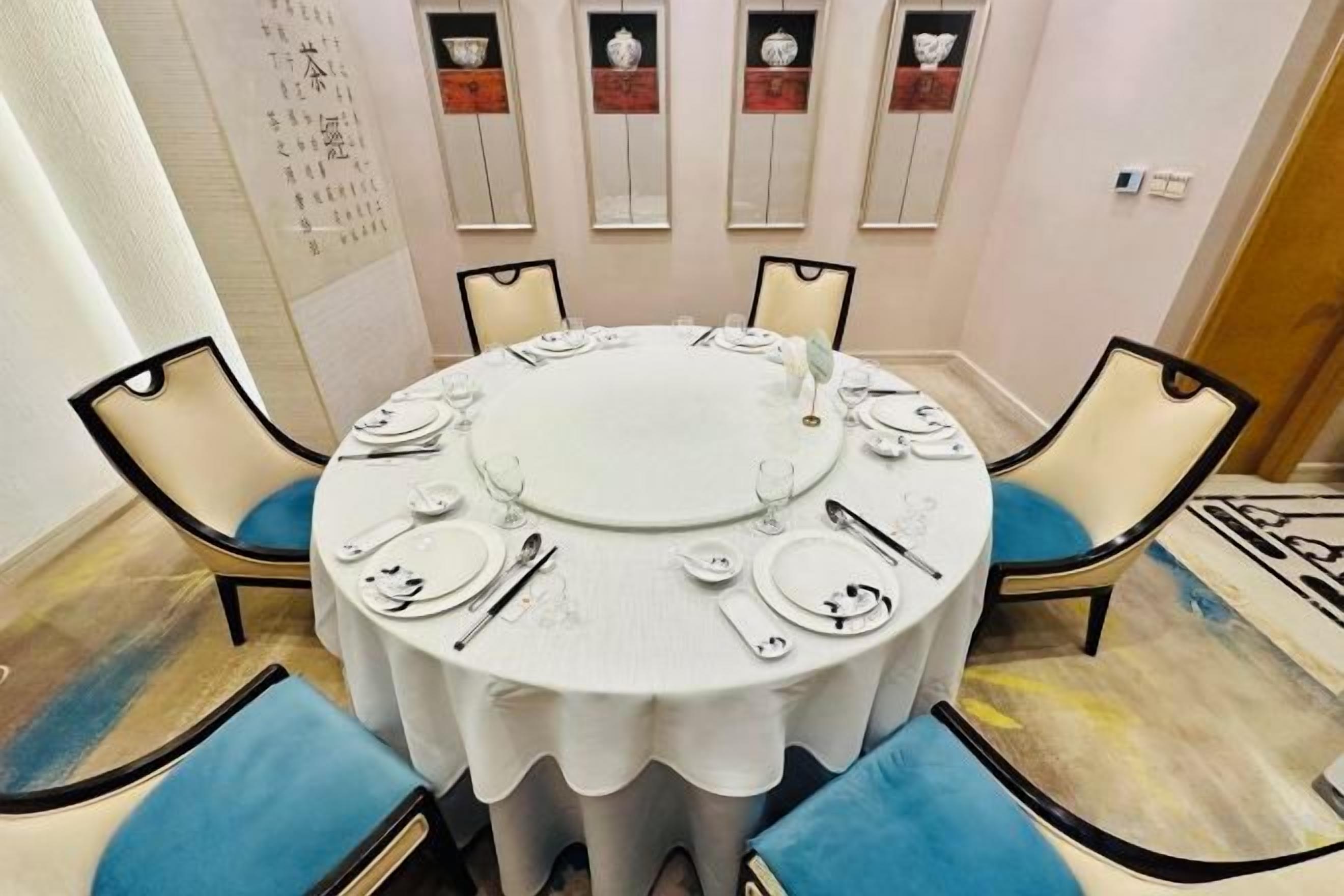 A round dining table with chairs, plates, and cutlery set for a meal.