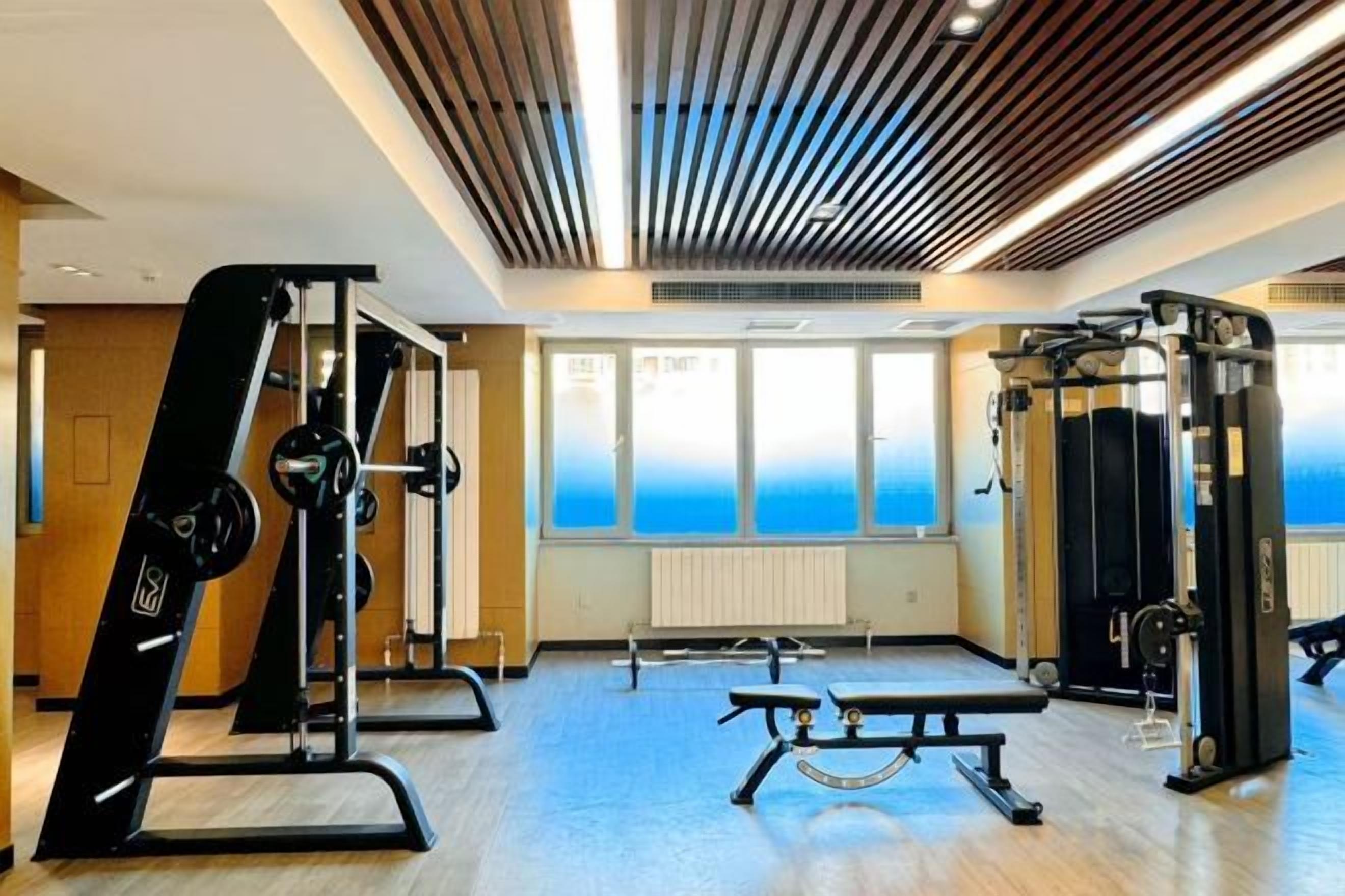 A gym with exercise equipment, large windows, and a wooden ceiling.