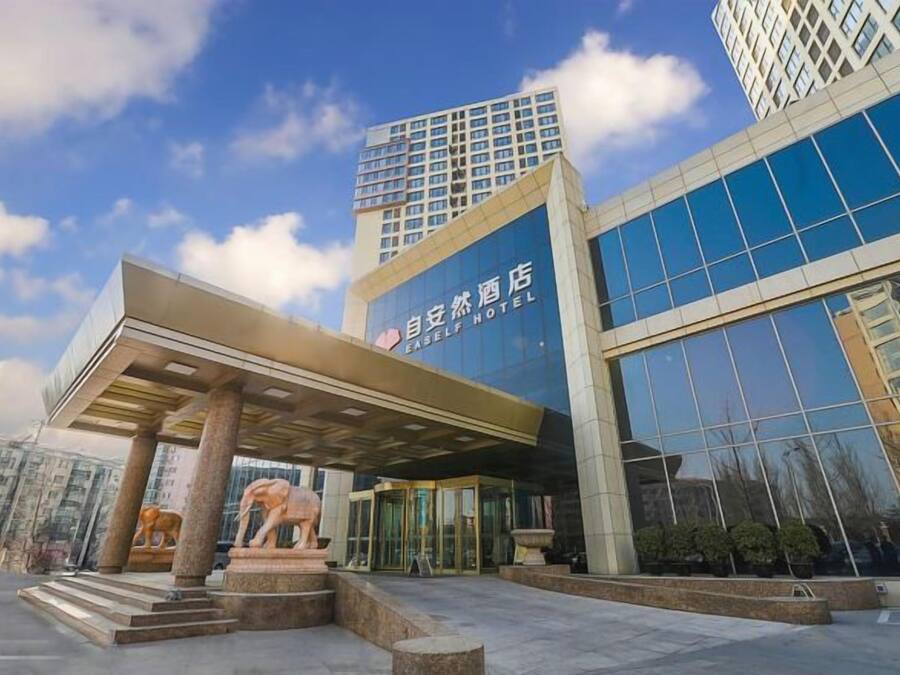 A modern hotel with a glass facade, a covered entrance, and a sculpture of a lion.