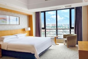 A hotel room with a large bed, a small desk, a chair, and a view of the city through large windows. - Eaself Hotel (Beijing)