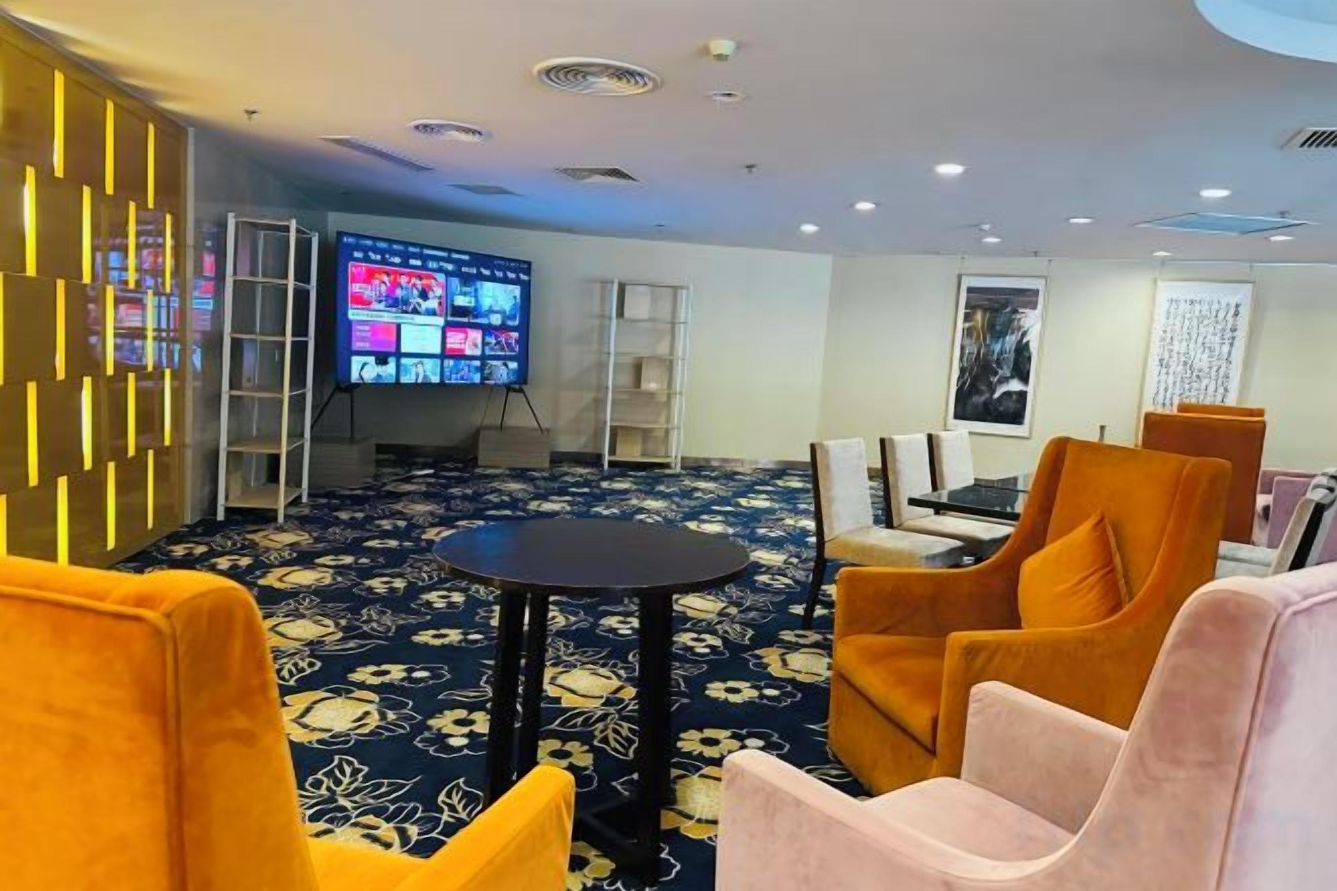 A hotel lobby with a large flat-screen TV, comfortable seating, and a patterned carpet.
