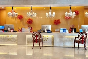 A hotel reception area with a reception desk, two computer monitors, a telephone, and a chandelier. - Eaself Hotel (Beijing)