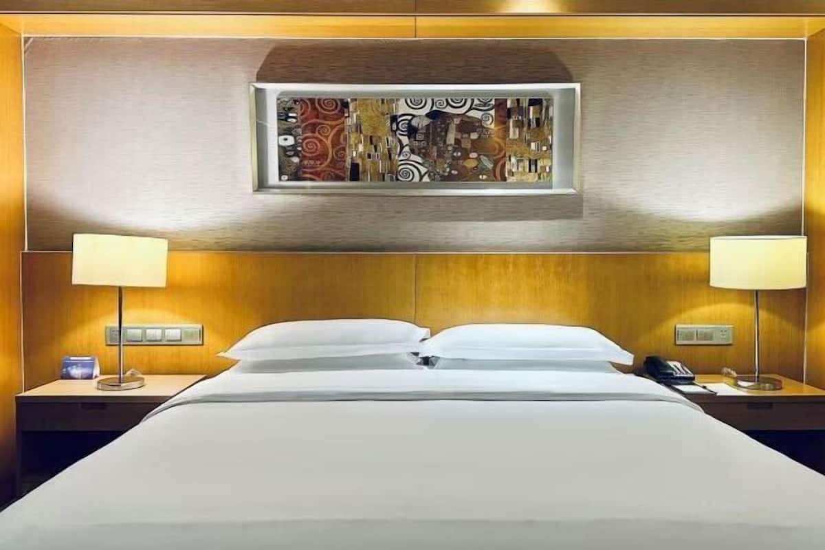 A hotel room with a bed, two bedside tables, lamps, a wall-mounted artwork, and a telephone.