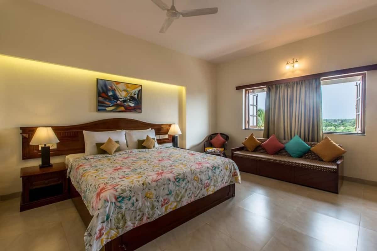 A hotel room with a large bed, a sofa, a ceiling fan, and a window with curtains.