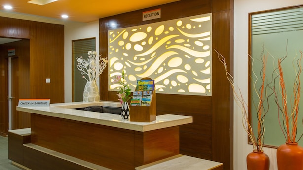 A reception area with a wooden reception desk, a ceiling fan, and a decorative wall panel. - Viva Hotel (Margao)