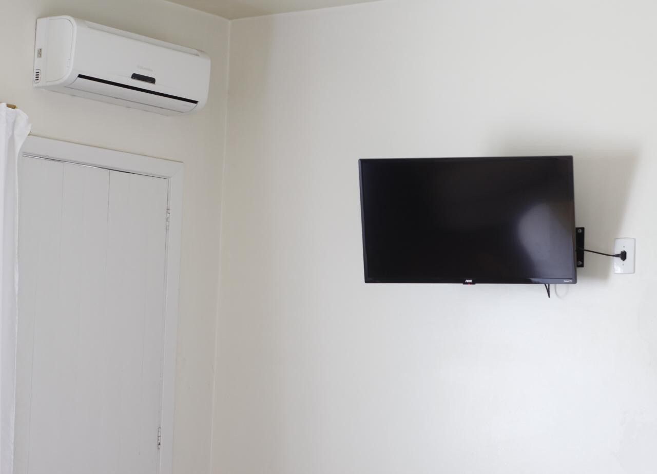 Une pièce avec une porte blanche, un climatiseur fixé au mur et un téléviseur à écran plat accroché au mur.