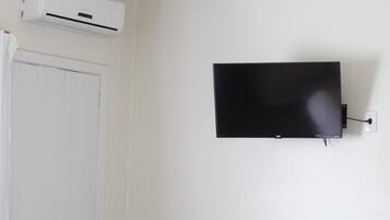 Une pièce avec une porte blanche, un climatiseur fixé au mur et un téléviseur à écran plat accroché au mur.