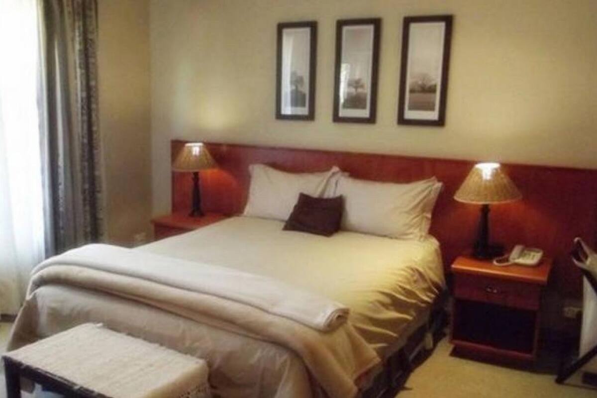 Habitación de hotel con una cama, dos mesitas de noche, una lámpara en cada mesita y una silla, además de un ventanal con cortinas.