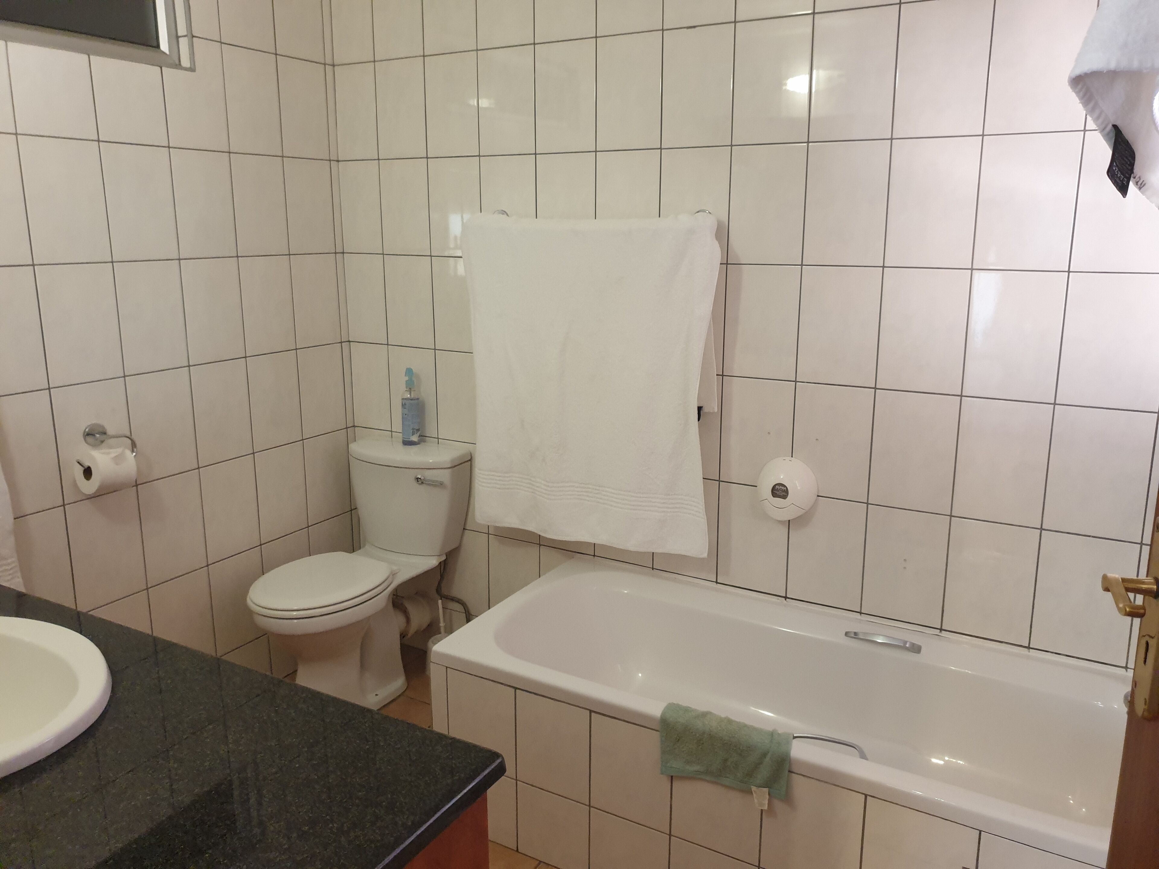 Een badkamer met witte tegels, een toilet, een wastafel en een bad.