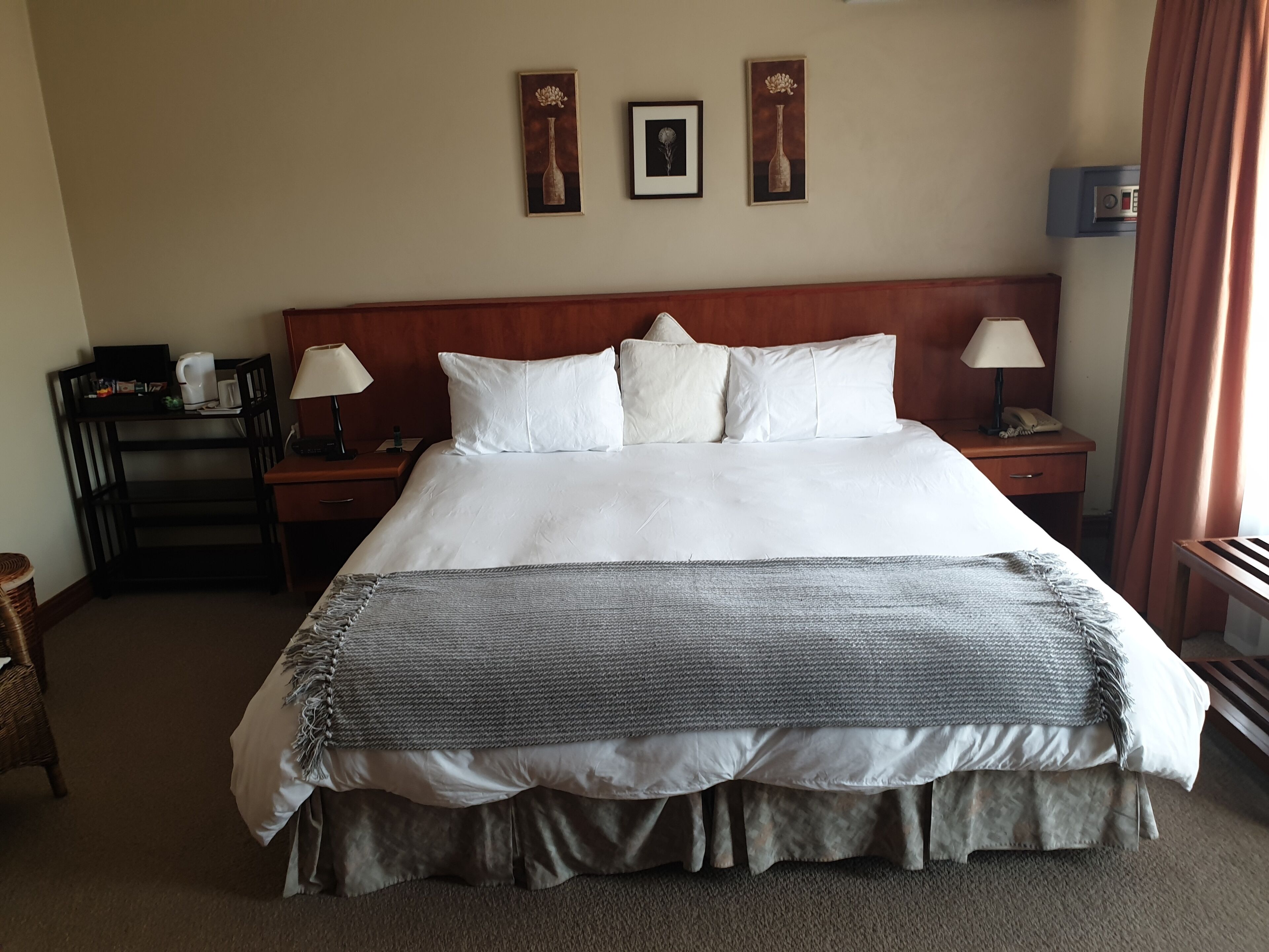Ein Hotelzimmer mit einem großen Bett, zwei Nachttischen, einem hölzernen Kopfteil und drei gerahmten Bildern an der Wand.