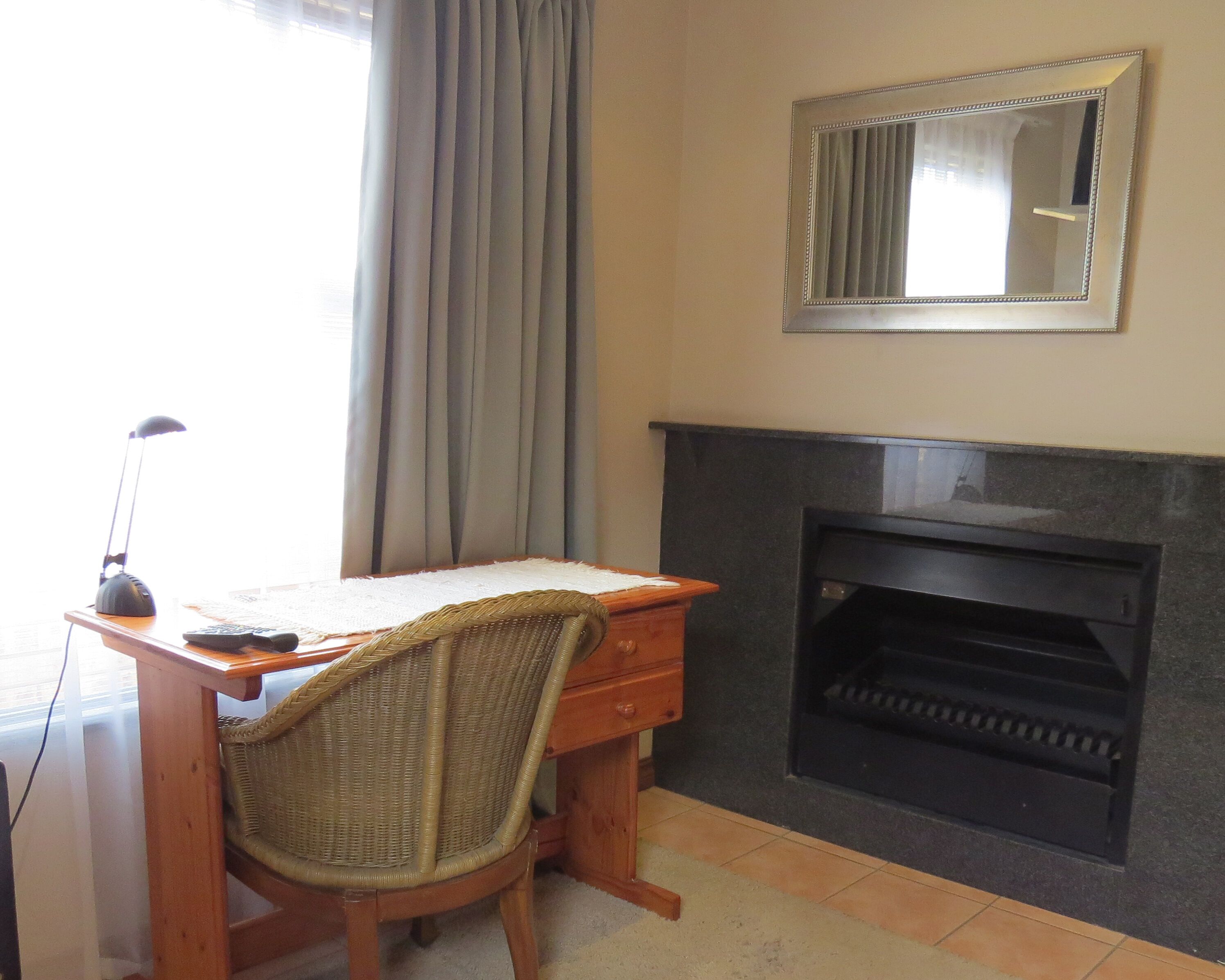 A room with a wooden desk, wicker chair, a mirror, and a fireplace.