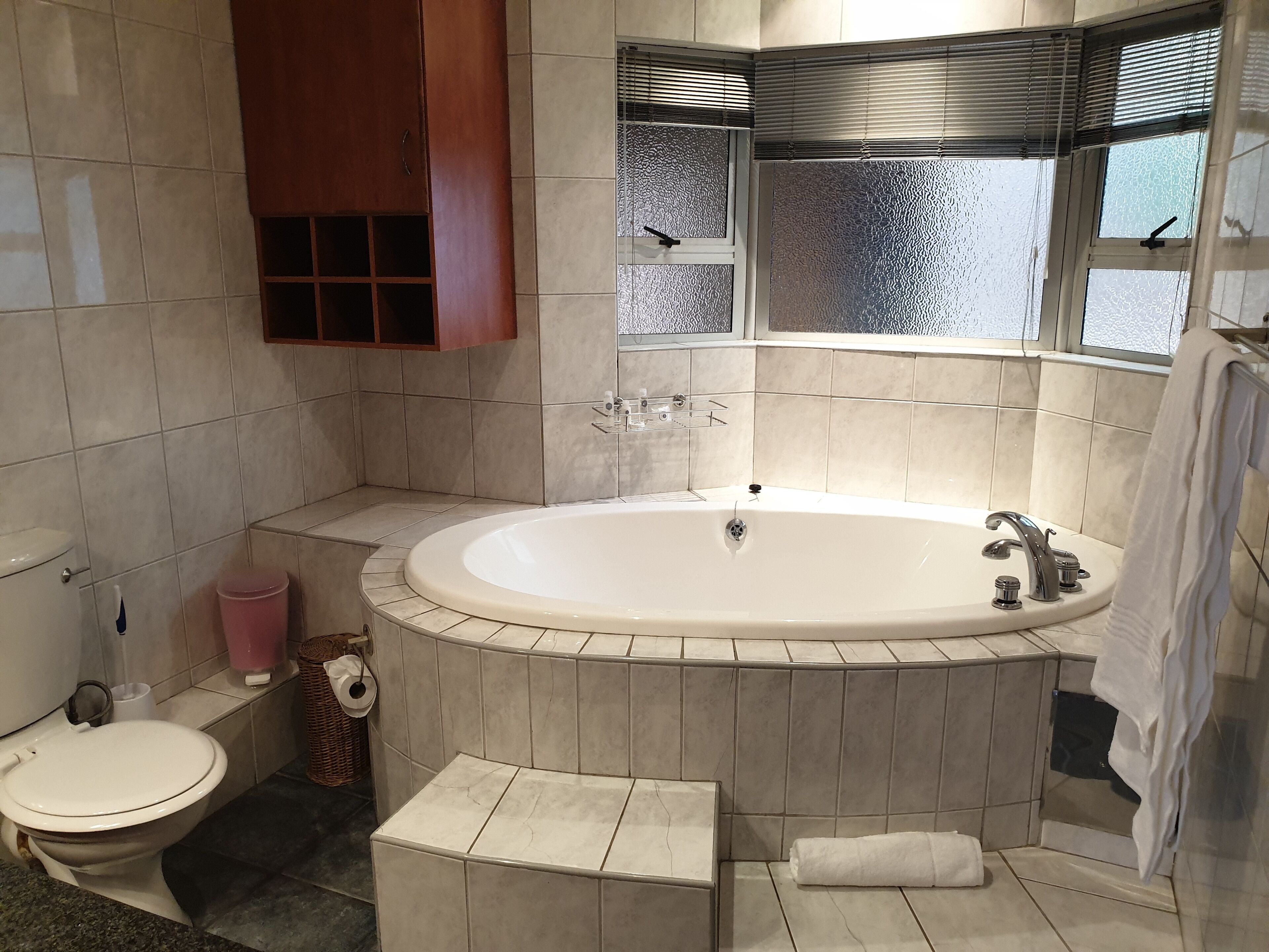 Een moderne badkamer met een vrijstaand bad, een toilet en een raam met zonwering.