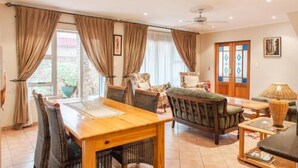 Un salón espacioso con una mesa de comedor de madera, asientos cómodos y ventanas grandes con cortinas.