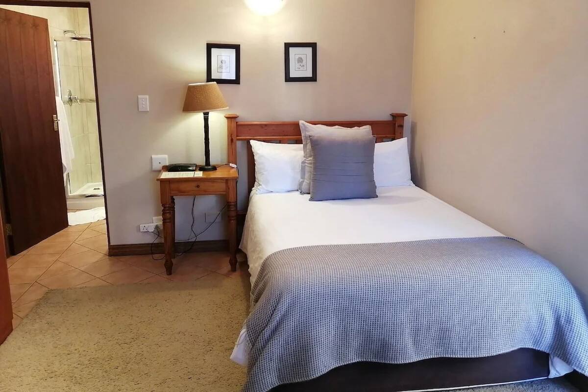 Habitación de hotel con una cama, una mesita de noche con lámpara, cabecero de madera y dos cuadros enmarcados en la pared.