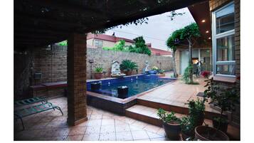Un espacio exterior techado con piscina, plantas en macetas y un muro de ladrillo.