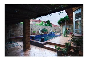 Un espacio exterior techado con piscina, plantas en macetas y un muro de ladrillo.