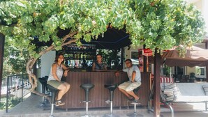A bar area with a wooden counter, black bar stools, and a canopy of grapevines overhead. - Melodi Club Hotel (Kusadasi)