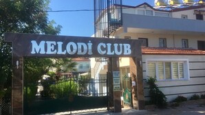 The entrance to Melodi Club with a gated driveway and a building in the background. - Melodi Club Hotel (Kusadasi)