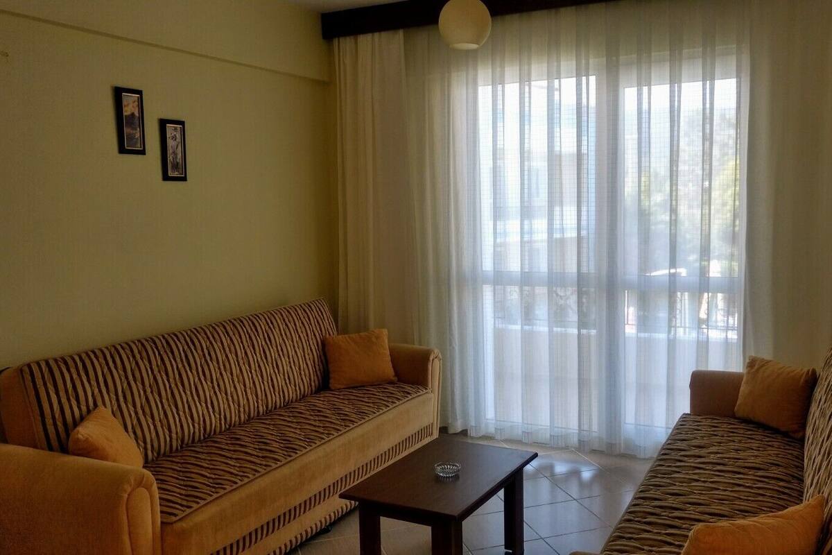 A living room with two sofas, a coffee table, and a large window with sheer curtains.