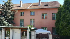 A pink building with multiple windows, a gated entrance, and a small outdoor seating area with tables and chairs. - Orbis (Prague)