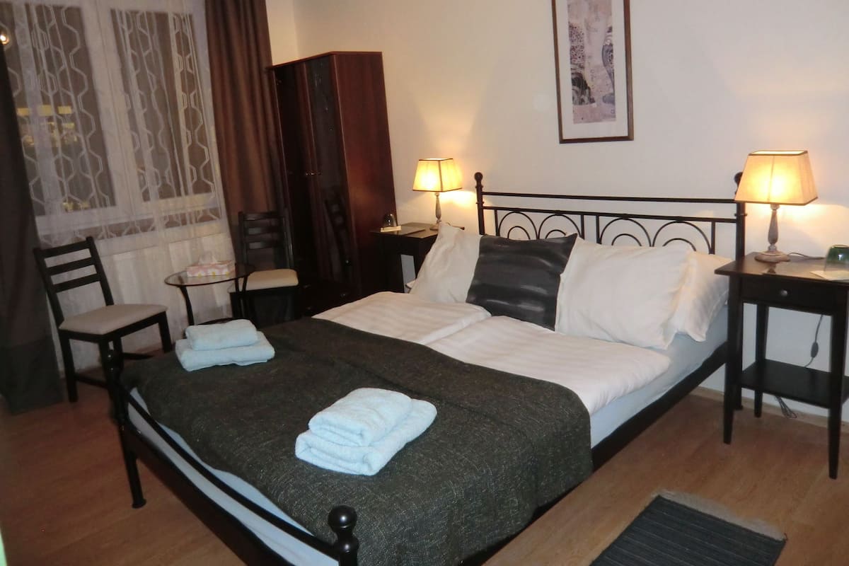 A neatly arranged hotel room with a bed, two bedside tables, a chair, a desk, and a wardrobe.