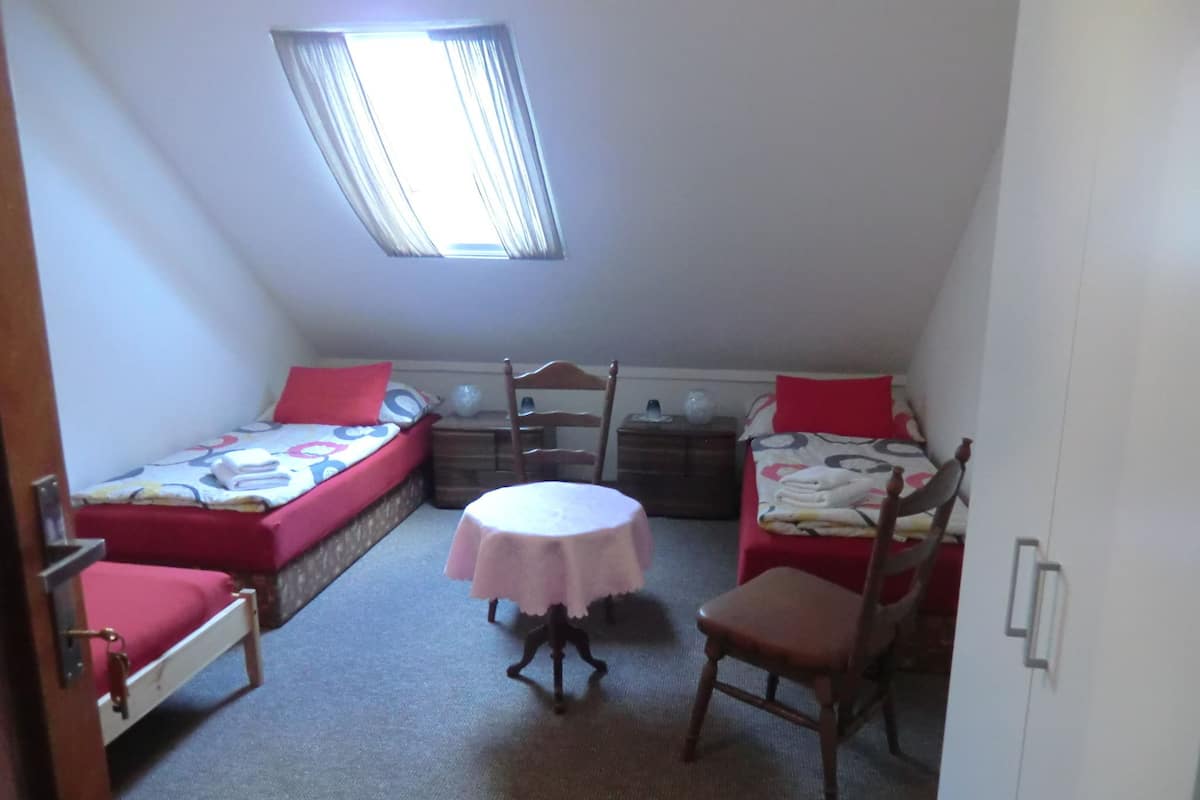 A small, triangular room with two single beds, a round table, and a chair.