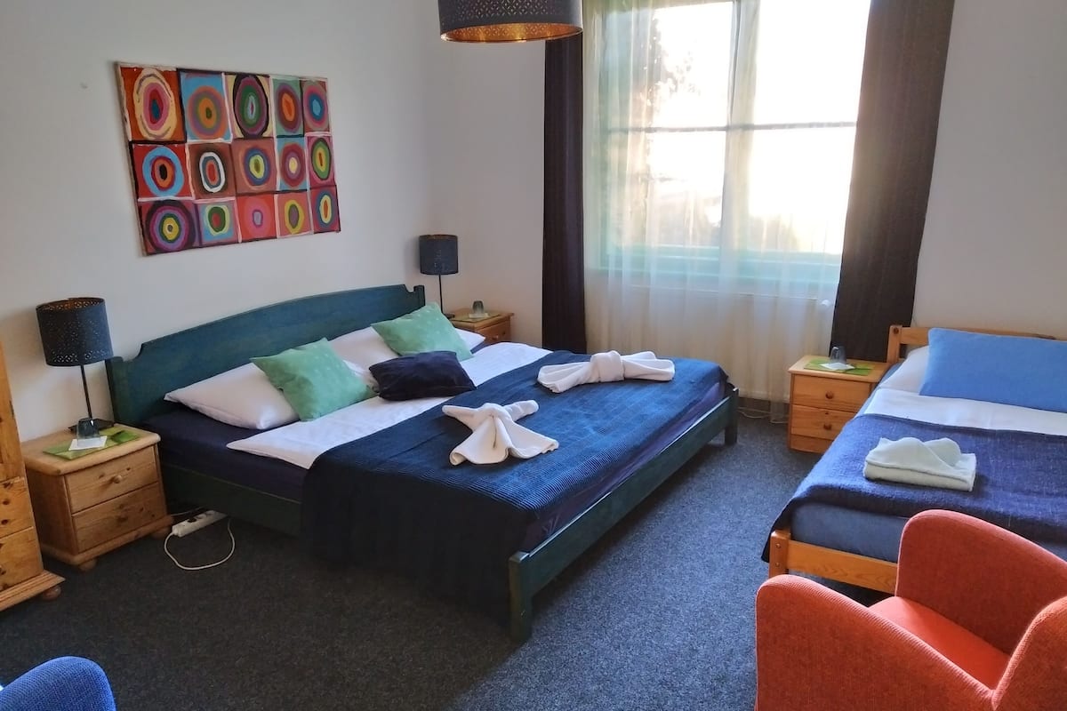 A hotel room with a large bed, two bedside tables, a desk, a chair, and a colorful abstract painting on the wall.
