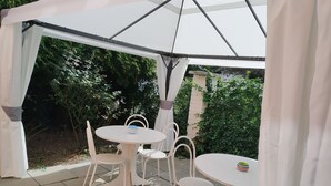 A covered patio area with white tables and chairs, surrounded by greenery. - Orbis (Prague)