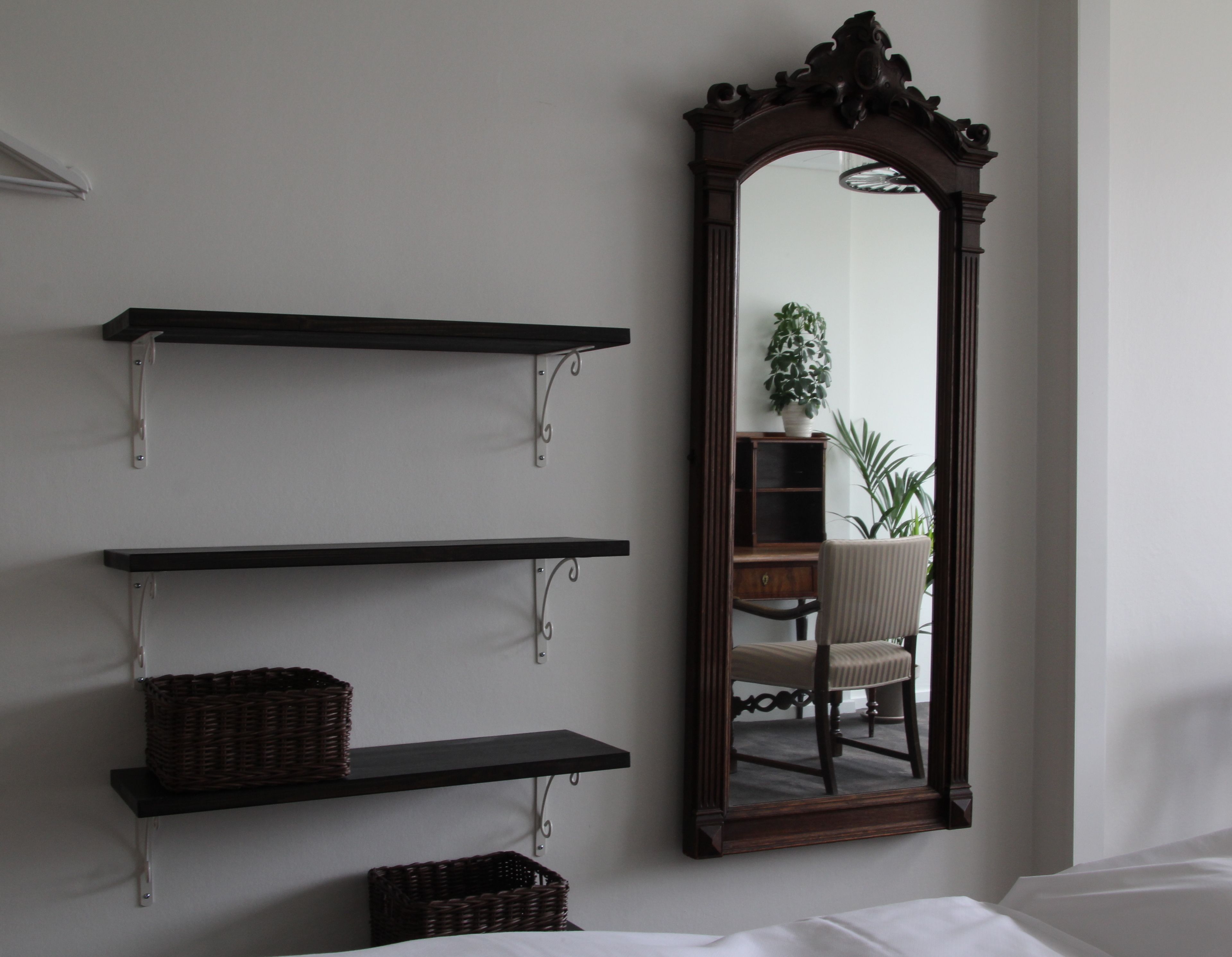 Una habitación con tres estantes negros, un espejo grande y una silla.