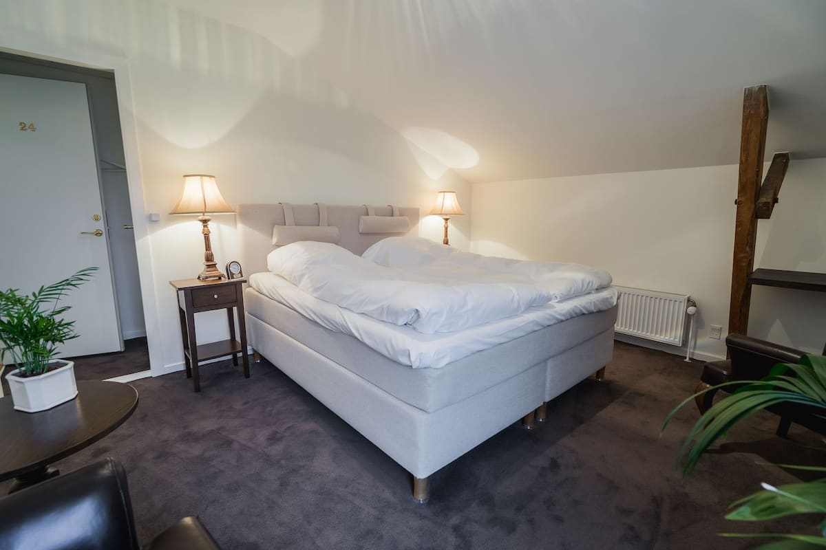 Ein Schlafzimmer mit einem Bett, Nachttischlampen, einem kleinen Tisch und einer Topfpflanze.