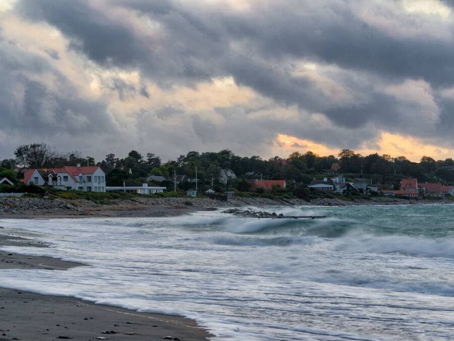 A coastal scene with a beach, waves, and houses in the background.