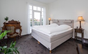 Un dormitorio con una cama grande, dos lámparas de noche, un escritorio de madera, una silla y vistas por una ventana.