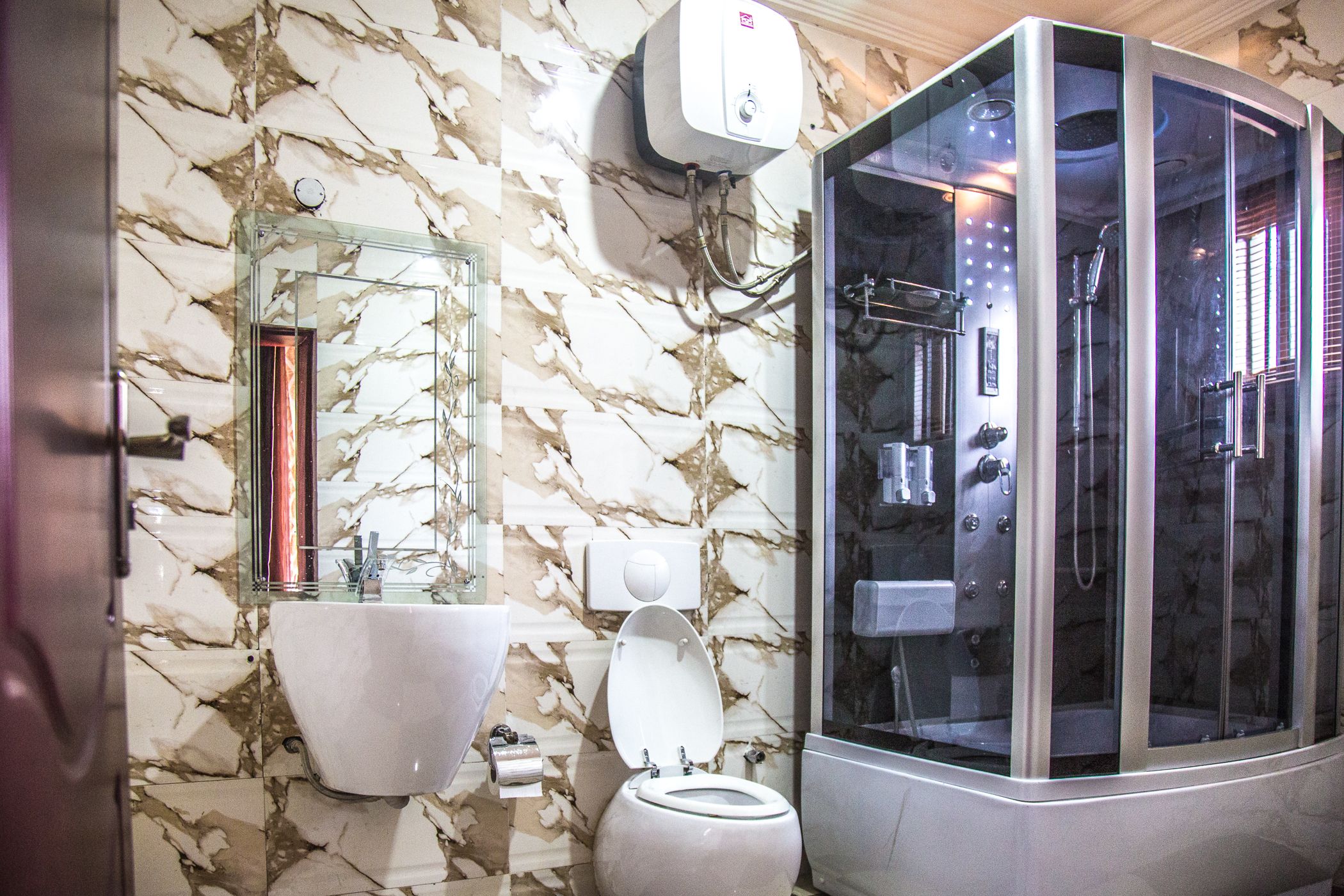 A bathroom with a marble wall, a glass-enclosed shower, a sink, and a toilet.
