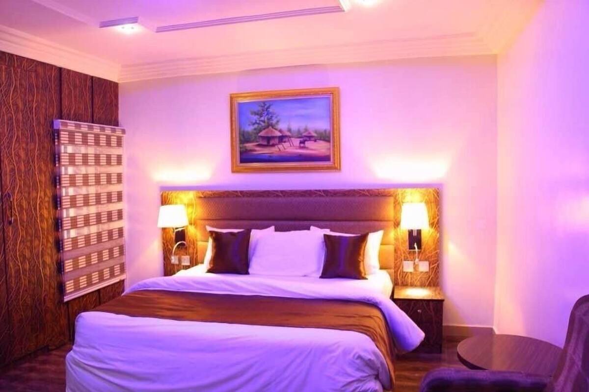 A hotel room with a large bed, two bedside lamps, a painting on the wall, and a small round table.