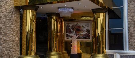 A grand entrance with golden columns, a chandelier, and a large painting.