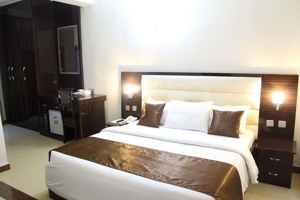 Une chambre d’hôtel avec un grand lit, des tables de chevet, une armoire et un bureau équipé d’un téléphone et d’un petit réfrigérateur.