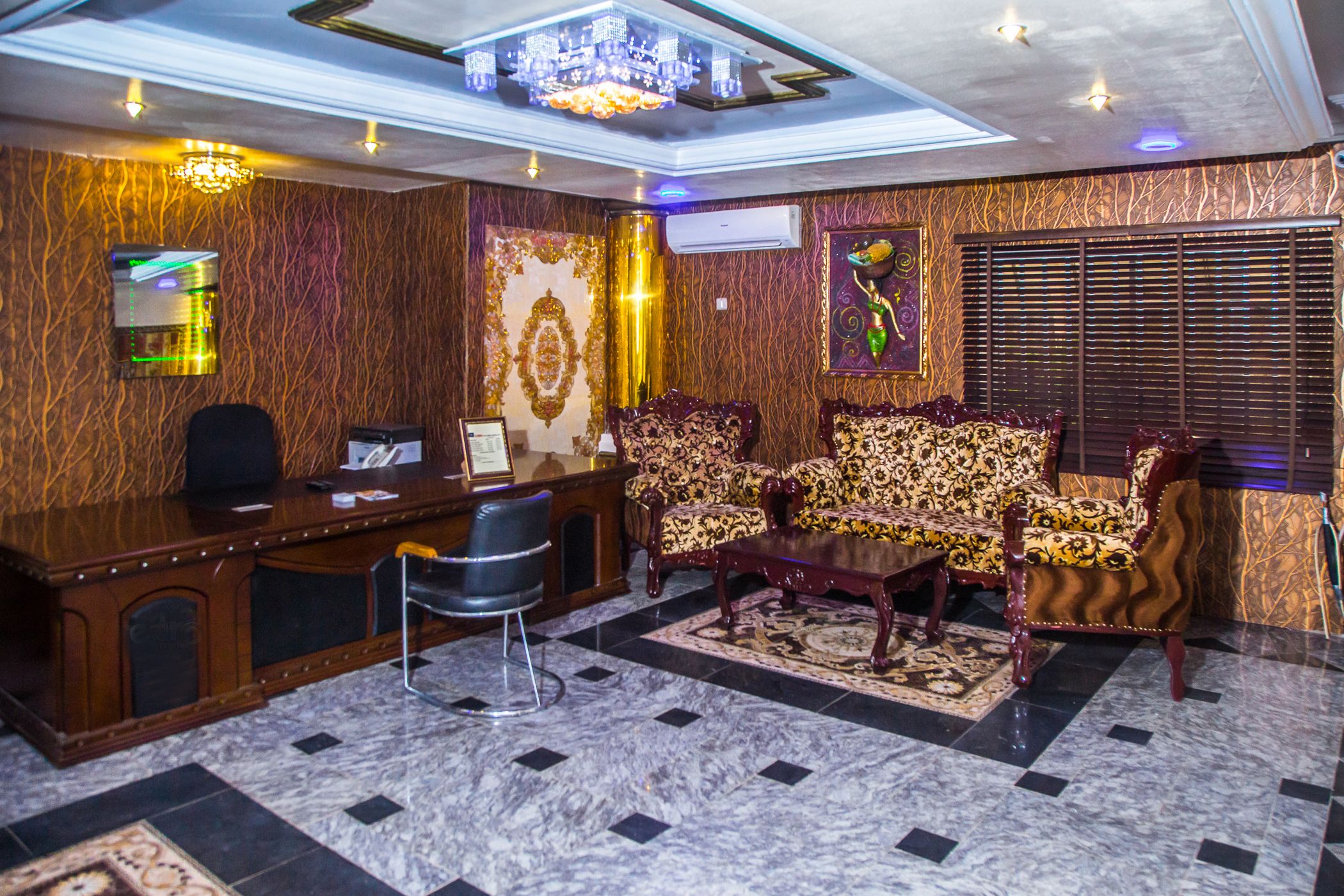 A conference room with a wooden reception desk, patterned sofas, a marble floor, and a chandelier.
